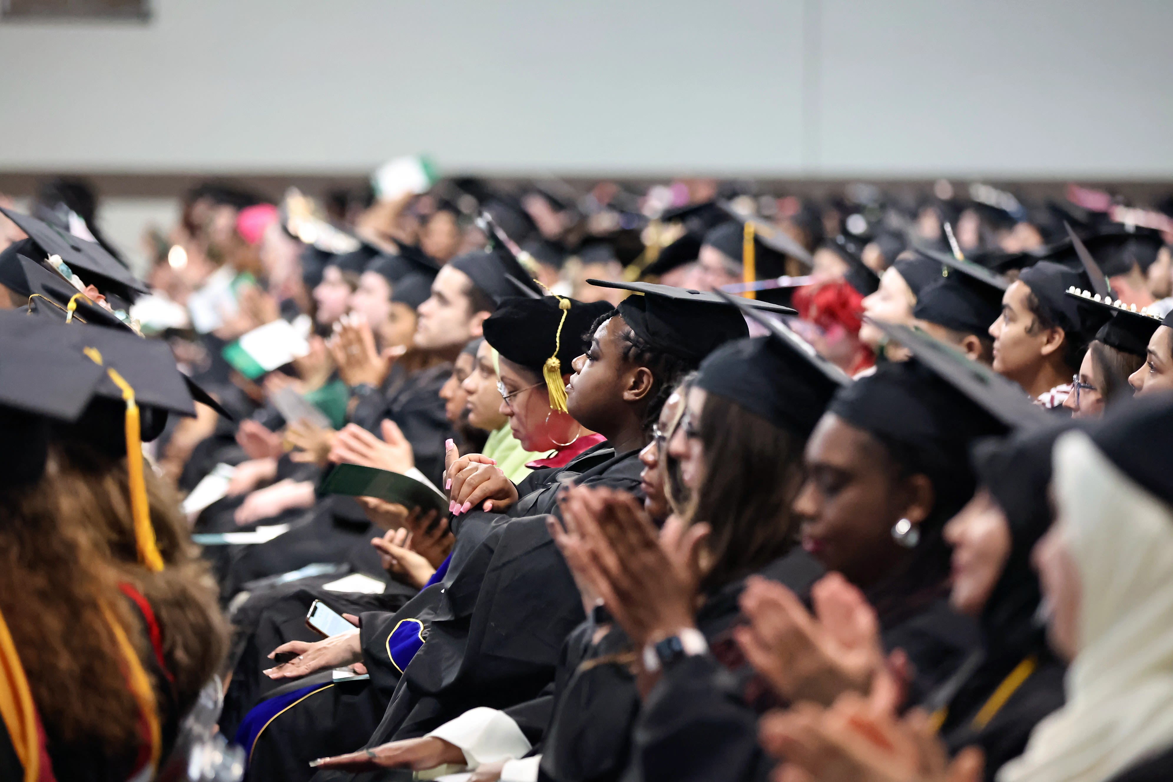A graduate in cap and gown holds a diploma outdoors.
