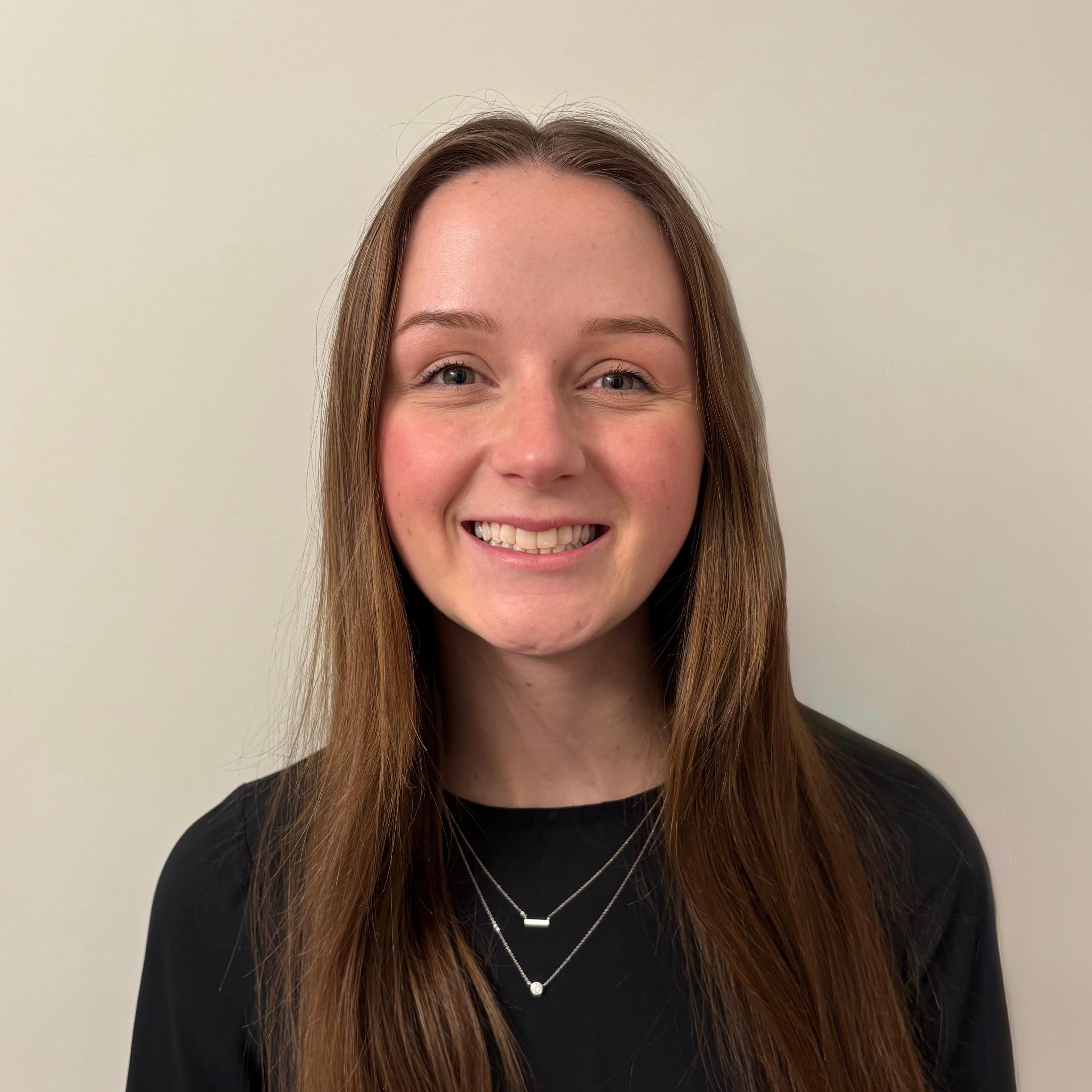 Graduation ceremony with graduates listening to a speaker in an indoor gymnasium setting.