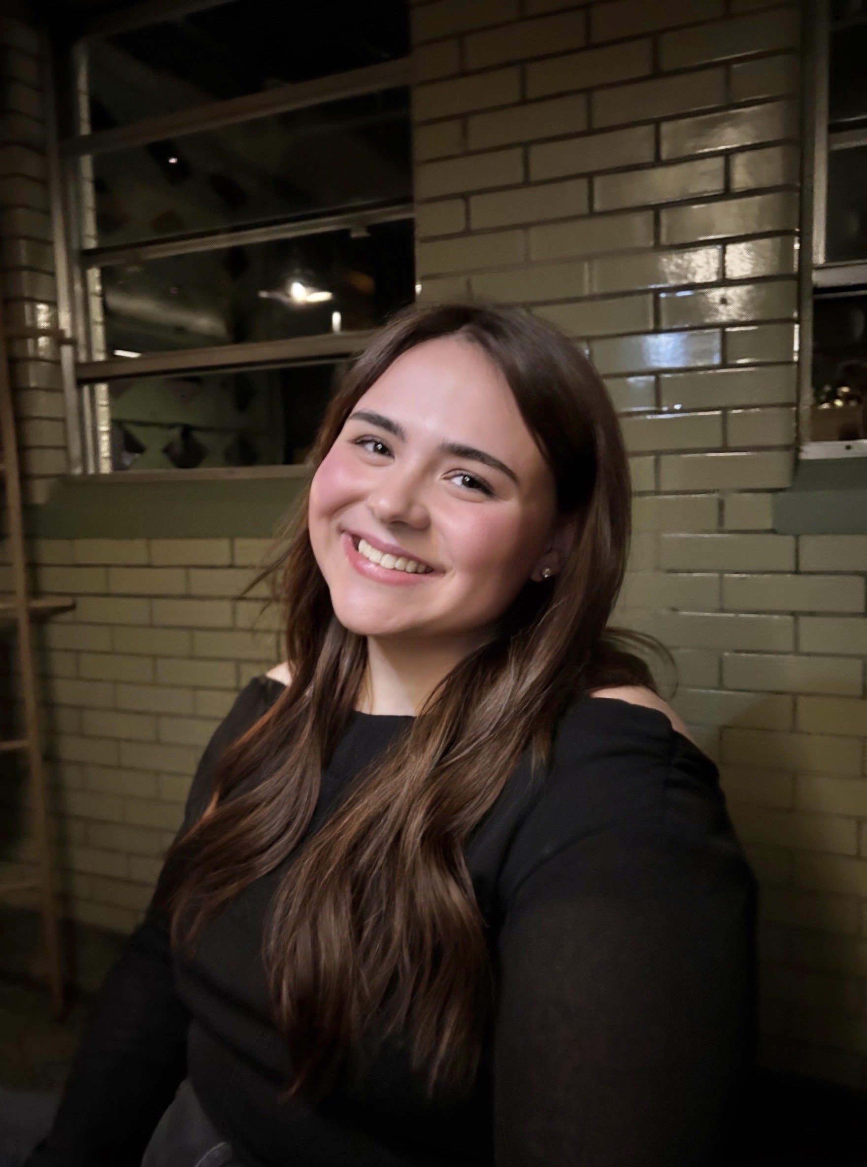Graduation ceremony with graduates listening to a speaker in an indoor gymnasium setting.