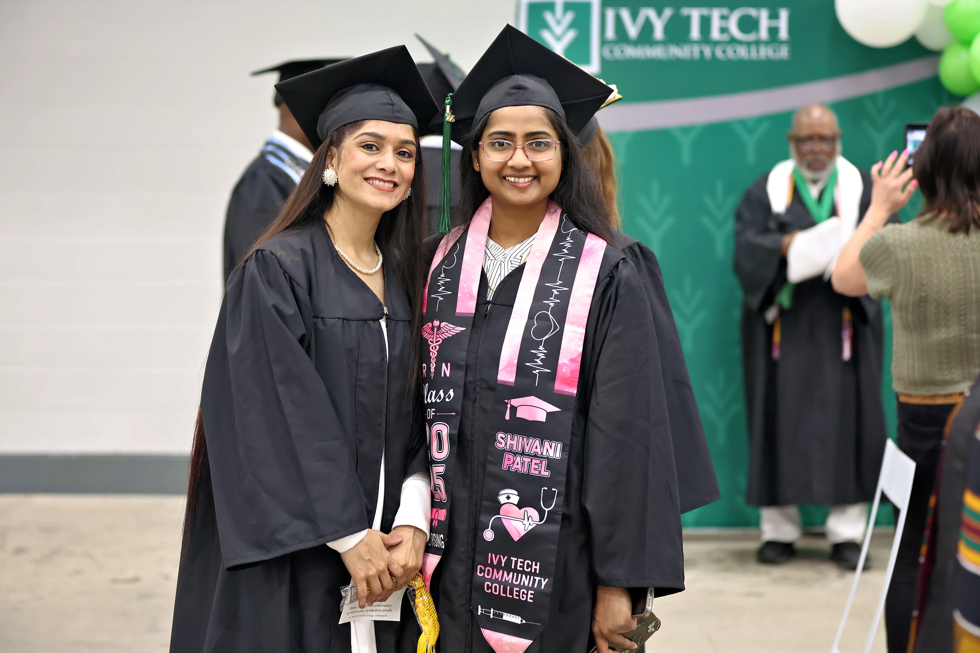 Graduation ceremony with graduates listening to a speaker in an indoor gymnasium setting.